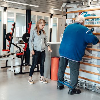 Rembrandt fysiotherapie & revalidatie- vacture - 65+ fysio en beweging Coen Fysiotherapeut Manon helpt Coen bij verschillende oefeningen in de oefenzaal fysiotherapie voor ouderen en 65 plus