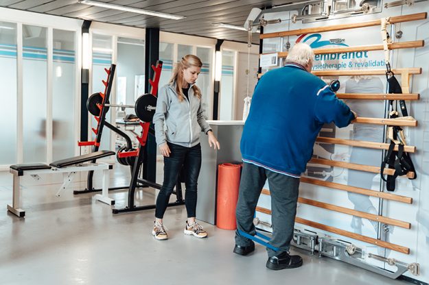 Fysiotherapeut Manon helpt Coen bij verschillende oefeningen in de oefenzaal fysiotherapie voor ouderen en 65 plus