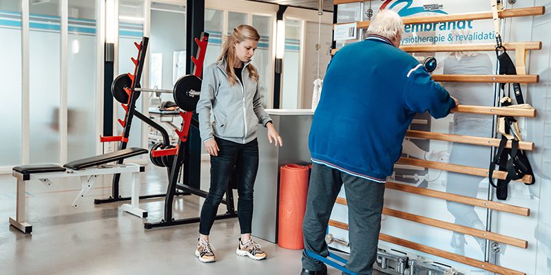 Rembrandt fysiotherapie & revalidatie- vacture – 65+ fysio en beweging Coen Fysiotherapeut Manon helpt Coen bij verschillende oefeningen in de oefenzaal fysiotherapie voor ouderen en 65 plus