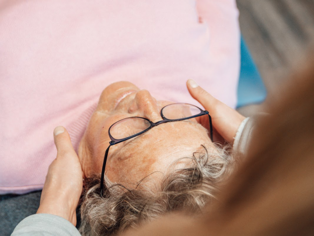 Vrouw in een roze shirt met bril op probeert met behulp van de fysiotherapie te slapen en haar hoofdpijn te verhelpen.