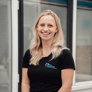 Profielfoto van Leoniek van Woudenberg die lachend naar de camera kijkt in een zwart shirt met logo.