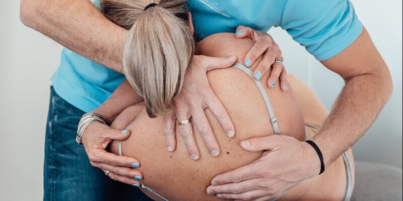 Manueel therapeut in een blauwe polo helpt een patiënt zonder shirt door middel van manuele therapie in Lienden bij chronische lage rugklachten en door de rug gaan.
