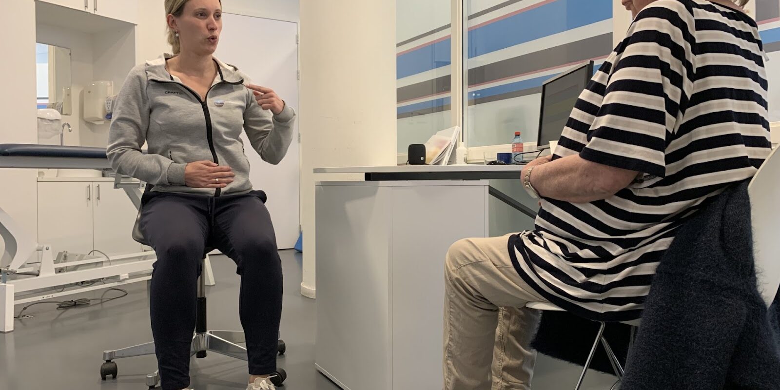 Patiënt in een gestreept shirt met longCOVID wordt geholpen door fysiotherapeut Rianne Doorn in een grijze polo