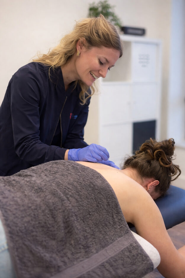 Fysiotherapeut past dry needling toe op bovenrug patient